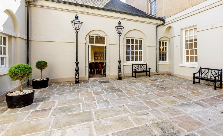 A tiled courtyard, with a bench and doorway to a registry office. The door has lampposts either side of it.